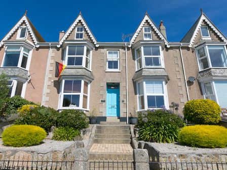 A row of houses with pointed roofs and a central blue door with stairs and garden beds at Waters Watch in St Ives