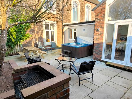 A backyard patio with chairs a table a picnic bench a hot tub and a brick barbecue at Grove House in Egremont
