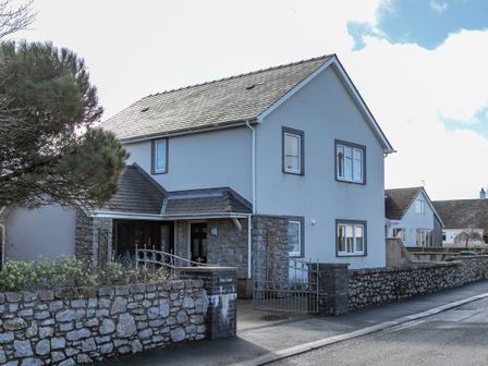 A two story house with gray walls and stone accents surrounded by a stone wall and metal gate at Pine Cones in Four Mile Bridge