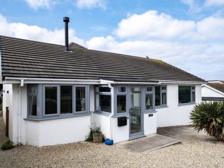 A single story house with grey framed windows a glass front door and a gravel driveway at Lowenda in Polzeath