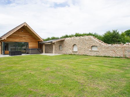 A lawn with a stone wall and a wooden building with glass doors at Owl Lodge in Wedmore