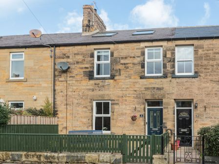A stone terraced house with blue door and green fence at 19 Duke Street in Alnwick