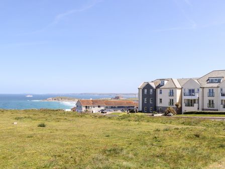 A grassy field with residential buildings near the coastline and ocean in the background at Penthouse 23 in Newquay