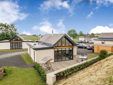 A view of modern houses with a wooden deck and outdoor seating in a rural area at Forget Me Not Lodge Bamburgh