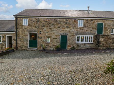 An outdoor view of a stone building with green doors at No 2 The Stables Capel Coch near Llannerch-Y-Medd