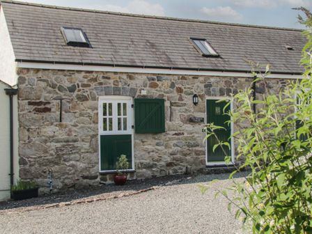 A stone building with green doors and windows and a gravel driveway at No 4 The Shippon Capel Coch near Llannerch-Y-Medd