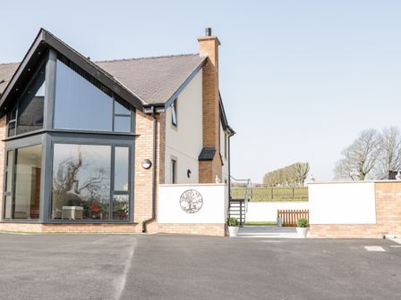 A house with large windows and a brick chimney next to a paved driveway at The Annexe in Llanfairpwllgwyngyll