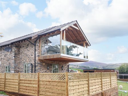 A stone building with a glass balcony and wooden fence with hills in the background at Tyn Y Ceubren Bach at Evelyns Retreat in Glyndyfrdwy