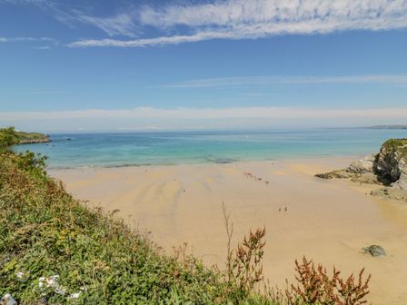 A sandy beach with people near the water and cliffs on both sides at 30 Cliff Edge in Newquay