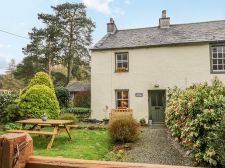 A cottage exterior with a wooden bench and picnic table in a garden at Nook Cottage in Rosthwaite near Keswick