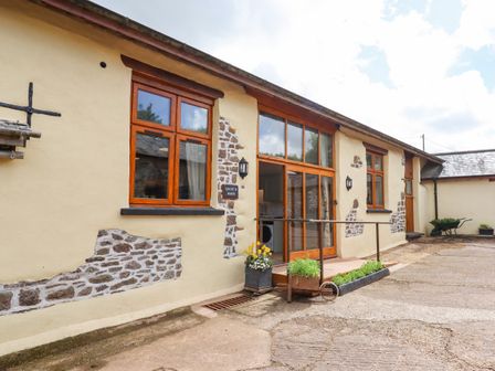 Exterior of a barn with wooden framed windows and doors with plants in front at Quoit X Barn in Stoodleigh near Bampton