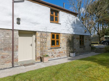 Exterior view of a stone and white plaster cottage with wooden framed windows and a beige door at The Annex - Trewolla Cottage in Trewolla near St Newlyn East