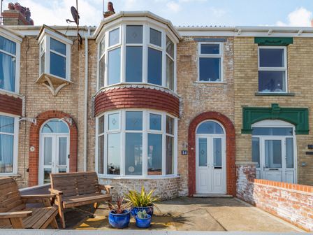 A row of brick houses with white doors and windows two wooden benches and three blue plant pots outside a house at 14 The Promenade Withernsea