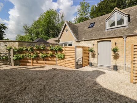 A gravel courtyard with wooden fences and potted plants outside a stone building at The Hayloft in Sherston
