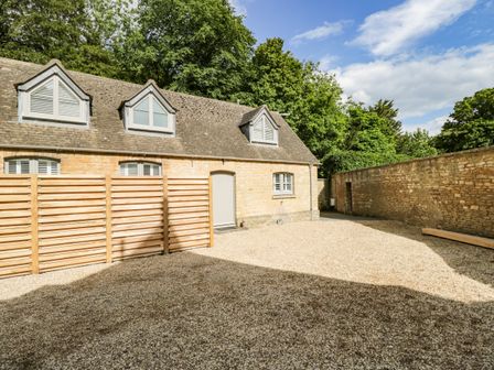 An outdoor gravel courtyard with a stone building and wooden fence at The Coach House in Westonbirt near Tetbury