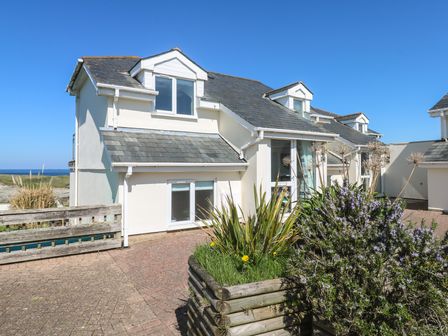 A white house with a slate roof and dormer windows along a paved driveway with plants in wooden planters at Island View in Porth