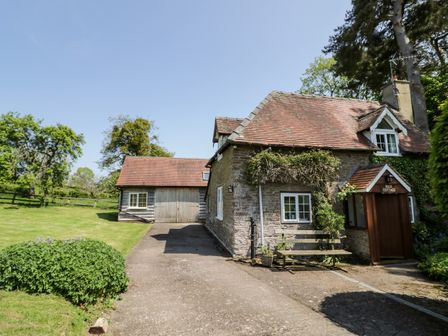 A stone cottage with a tiled roof and wooden porch beside a driveway and garden at Rock Cottage in Hatfield near Tenbury Wells
