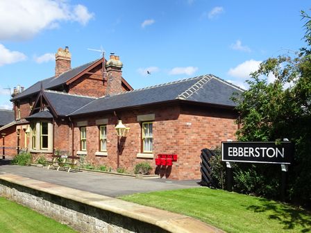 A brick building with multiple chimneys and windows next to a sign that says Ebberston