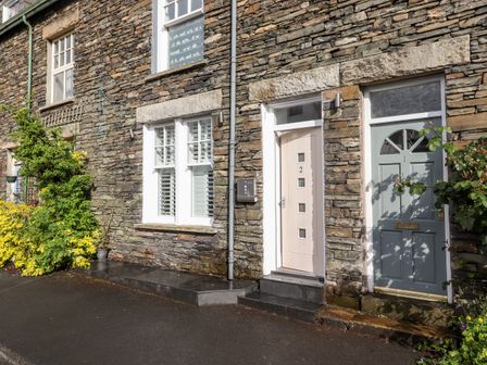 Stone exterior of two adjoining houses with white framed windows and numbered front doors at 2 Alexandra Road in Windermere