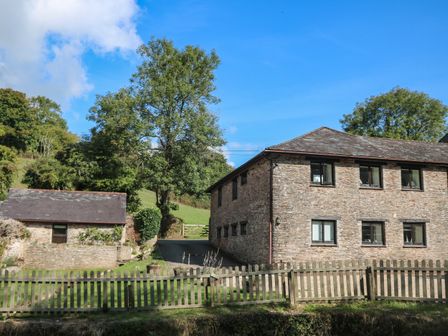 A stone house and a smaller stone building next to a wooden fence in a grassy area with trees at Primrose at Stancombe Manor Nr Kingsbridge Sherford