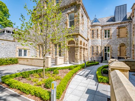 Exterior courtyard of a stone building with arched entrances and a paved walkway surrounded by trimmed hedges and a tree at Alice House Stone Cross Mansion in Ulverston