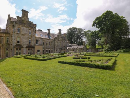 A large stone mansion with a manicured garden and hedges in front at The Violet Suite Stone Cross Mansion in Ulverston