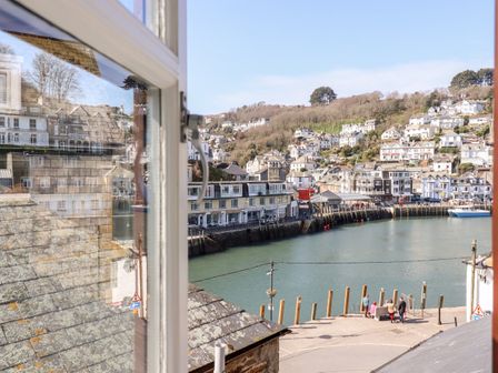 A harbor with boats houses on hillside and people near water viewed through a window at Smugglers Loft in Looe