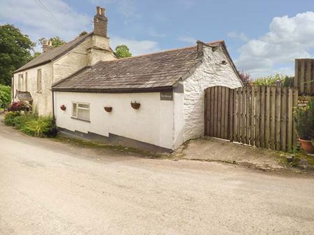 A white stone house with a tiled roof and wooden gate by a road at The Retreat in St Keyne near Liskeard