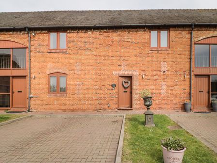 A brick building exterior with brown doors and windows and potted plants in front at The Wheat House in Welford-On-Avon