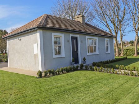 A small house with a tiled roof and a lawn with shrubs at An Teachain in Adamstown County Wexford