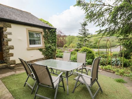 An outdoor patio with a glass table and six chairs next to a house with ivy on the wall at Swaledale Watch House Annexe in Caldbeck