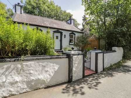 A white cottage with black trim and a small garden behind a low white wall with a black gate at Carreg Winllan in Llaneilian near Amlwch