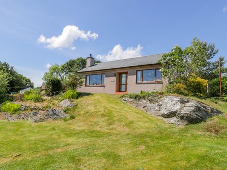 A house with a grass lawn and rocks in front at Ceris in Penrhyndeudraeth