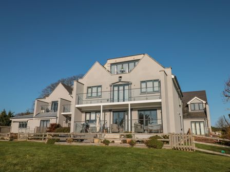 A large modern house with balconies and glass railings overlooking a grassy lawn at Seaspray Stoke Fleming Near Dartmouth