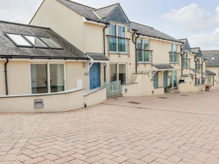 A row of modern townhouses with blue doors and glass balconies on a paved street at Constantine Bay Cottage in Constantine Bay
