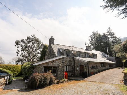 A stone house with multiple windows and chimneys surrounded by trees and bushes at Gilfachwydd Islawrdref near Dolgellau