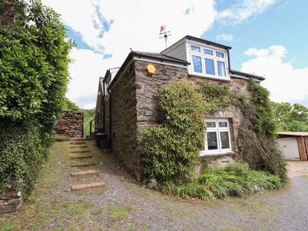 Stone house with climbing plants and driveway with bush on the side at Bodowen Coach House in Abermo near Barmouth