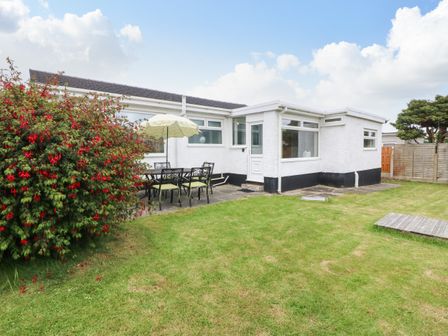 A backyard with a table and chairs under an umbrella next to a white house with a garden at H Jem in Benllech