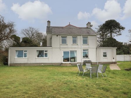 The back view of a two-story house with a grassy yard and an outdoor table with six chairs at Dolafon in Morfa Nefyn