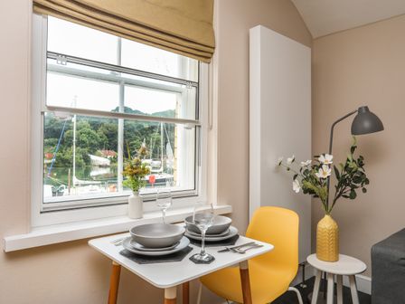 A dining area with a small table set for two near a window with a view of boats on water at Cwm Gwyrfai in Caernarfon
