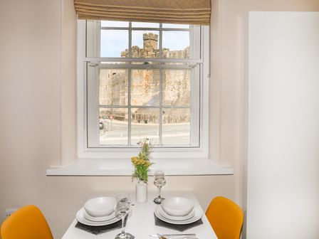 A dining table set for two with white dishes and glasses near a window showing a stone castle outside at Moel Tryfan in Caernarfon
