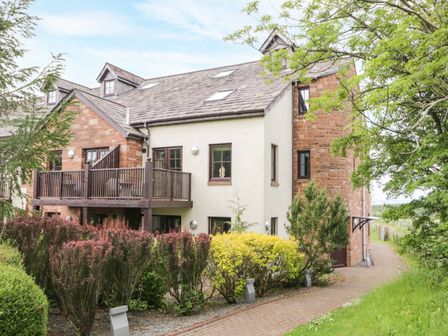 A residential building with a balcony surrounded by bushes and trees at Cosy Corner in the Lakes Greystoke