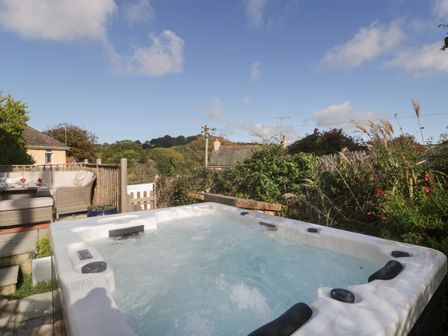 An outdoor hot tub and seating area with wicker furniture in a garden setting at Pound Cottage in Uplyme