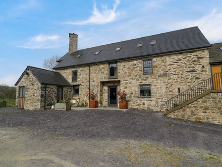Stone house with multiple windows and a small patio at Plas Glan Yr Afon in Llangernyw