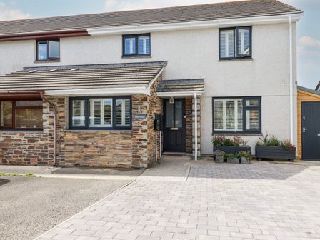 The exterior front view of a two-story semi-detached house with a paved driveway and flower planters at Trelowen in St Issey near Padstow