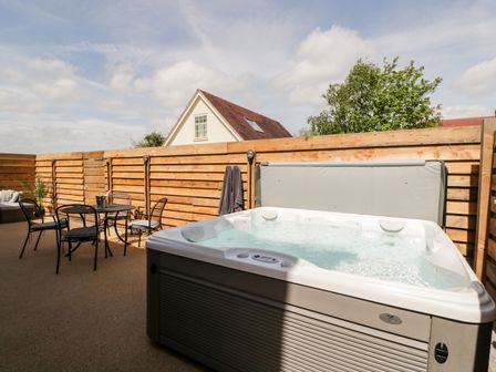 An outdoor patio with a hot tub a round table with four chairs and wooden fencing at Little Lugg in Cross Keys near Hereford
