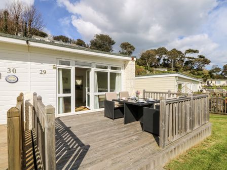 A wooden deck with a table and chairs outside a white cabin with large windows at Seas The Day in Ventnor