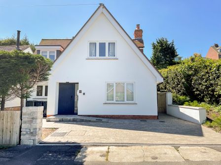 A white house with a peaked roof a black front door and paving in front at Lobster Lookout in Swanage