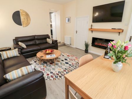 A living room with two brown sofas a round wooden coffee table and a wooden dining table with flowers at Stone's Throw in Amble