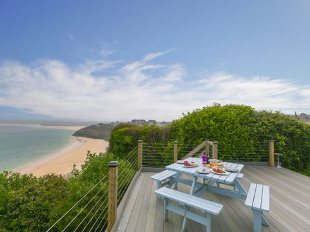 An outdoor deck with a picnic table set with food and plates overlooking a beach and ocean at Moonbeams in Carbis Bay
